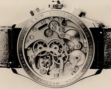 Macro view of the transparent case back of a Leica wristwatch, revealing the intricate mechanical movement, gears and engraved details.