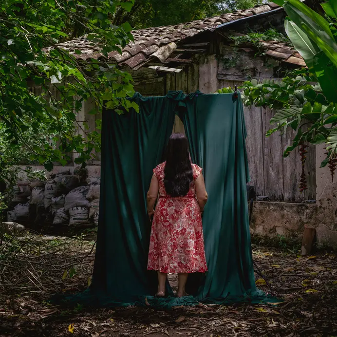 Woman in the forest walks through a green curtain behind a forest house