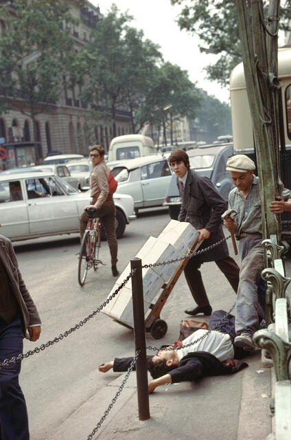A young man in a suit and tie lies on his back with arms stretched above his head, directly next to the metro station