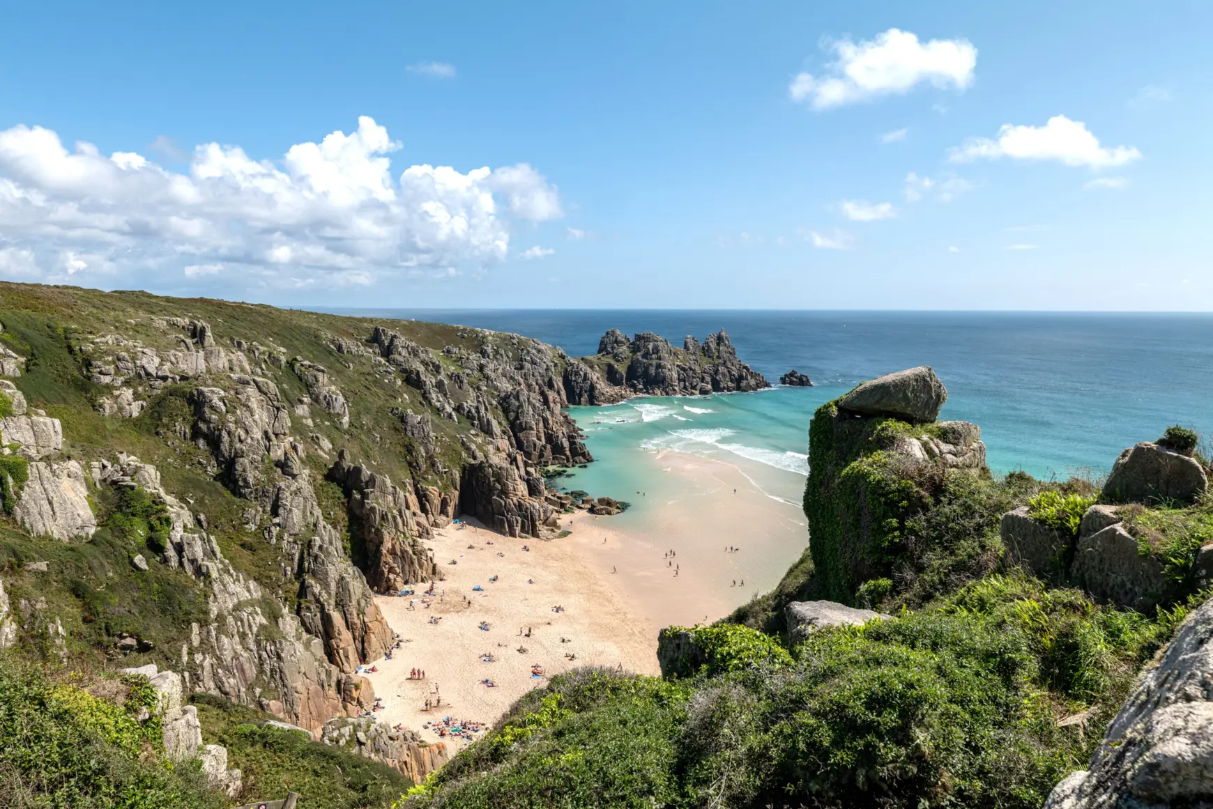 Small beach with sand and turquoise water between small rocks.