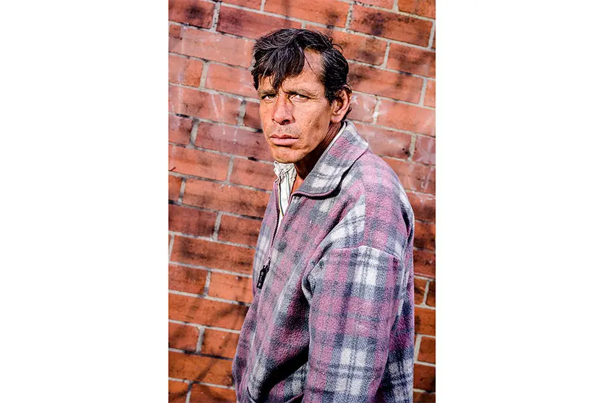 Man with a purple jacket in front of a brick wall