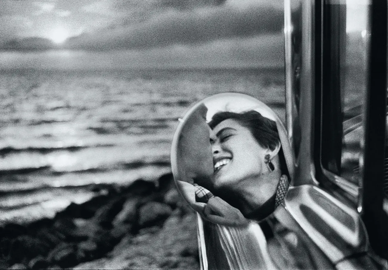 A couple kissing, captured through a wing mirror in front of the sea.