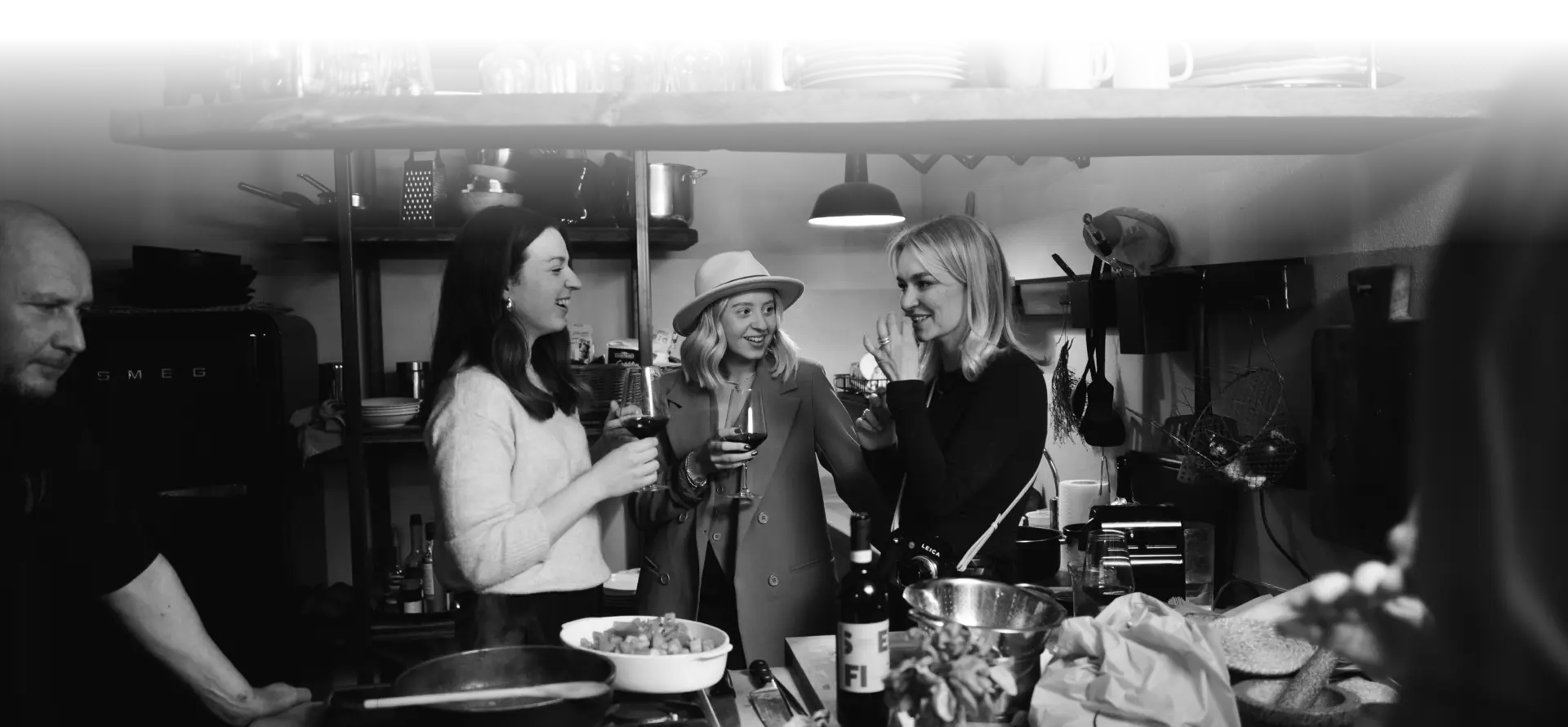 Three women with a wine glass in their hands stand in a kitchen