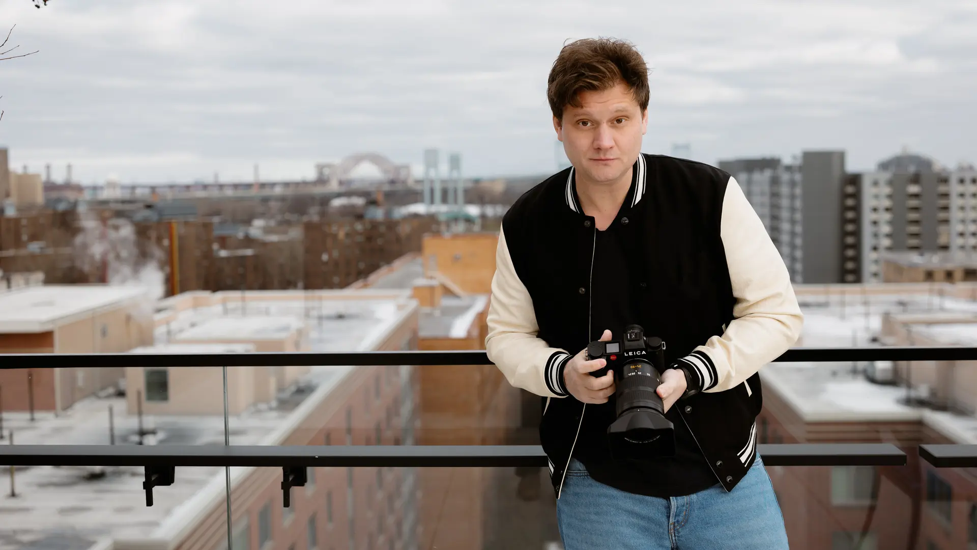 Person holding a camera, in the background are skyscrapers and a bridge on a cloudy day.