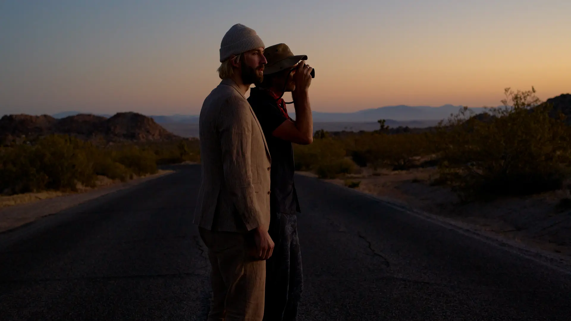 Garrett and Gantry Hill in a desert landscape at sunset, one looking through a camera.