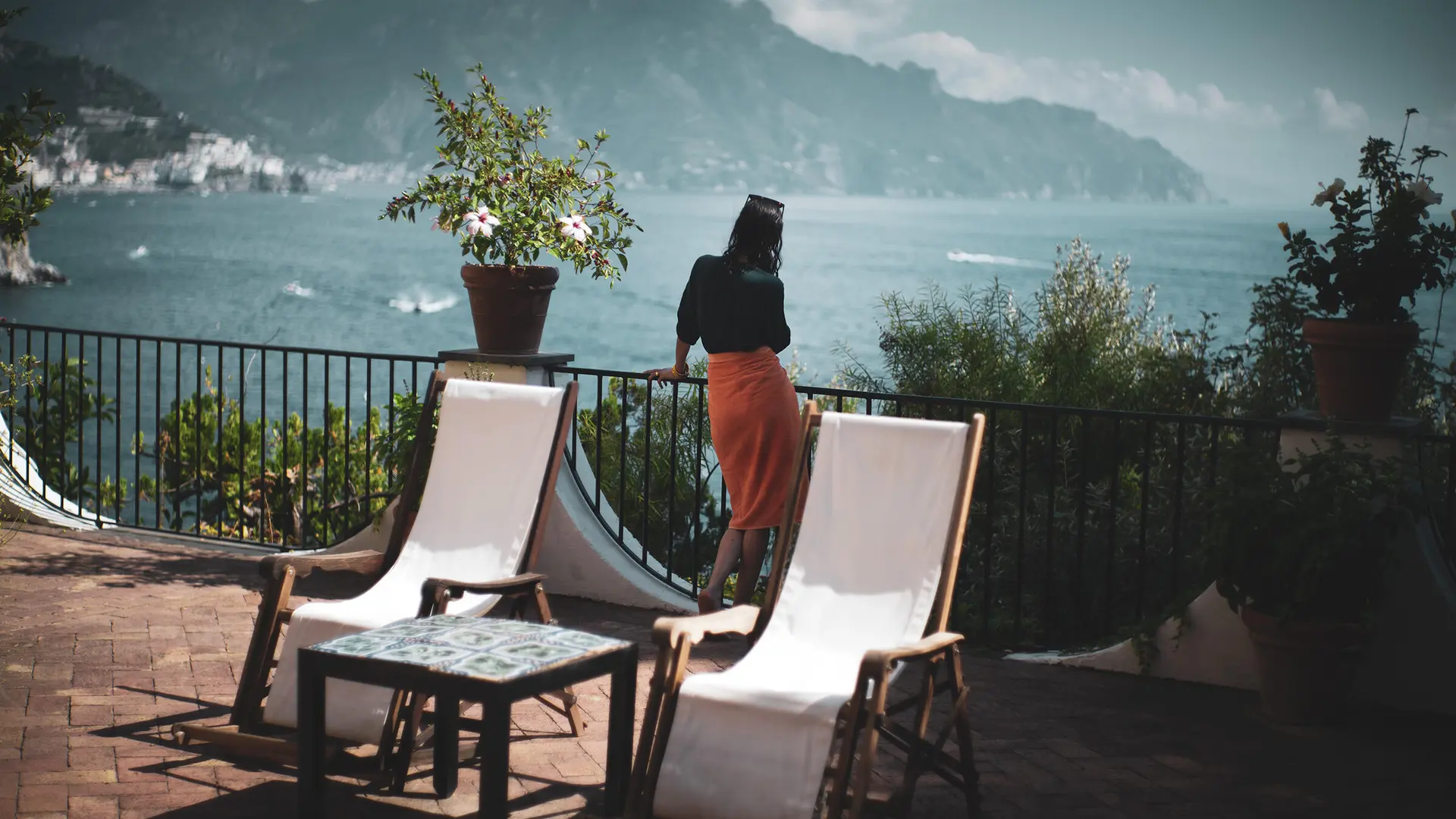 Woman on a large balcony with a view of a lake and mountains.