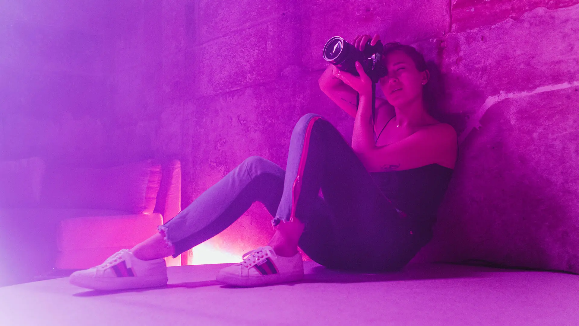 Alex Drewniak sits on the floor, taking pictures in a room lit by pink-purple light.