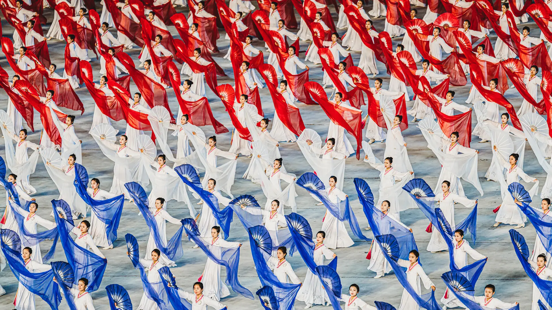 North Korean women dance with hand fans and transparent cloths in white, red and blue. 