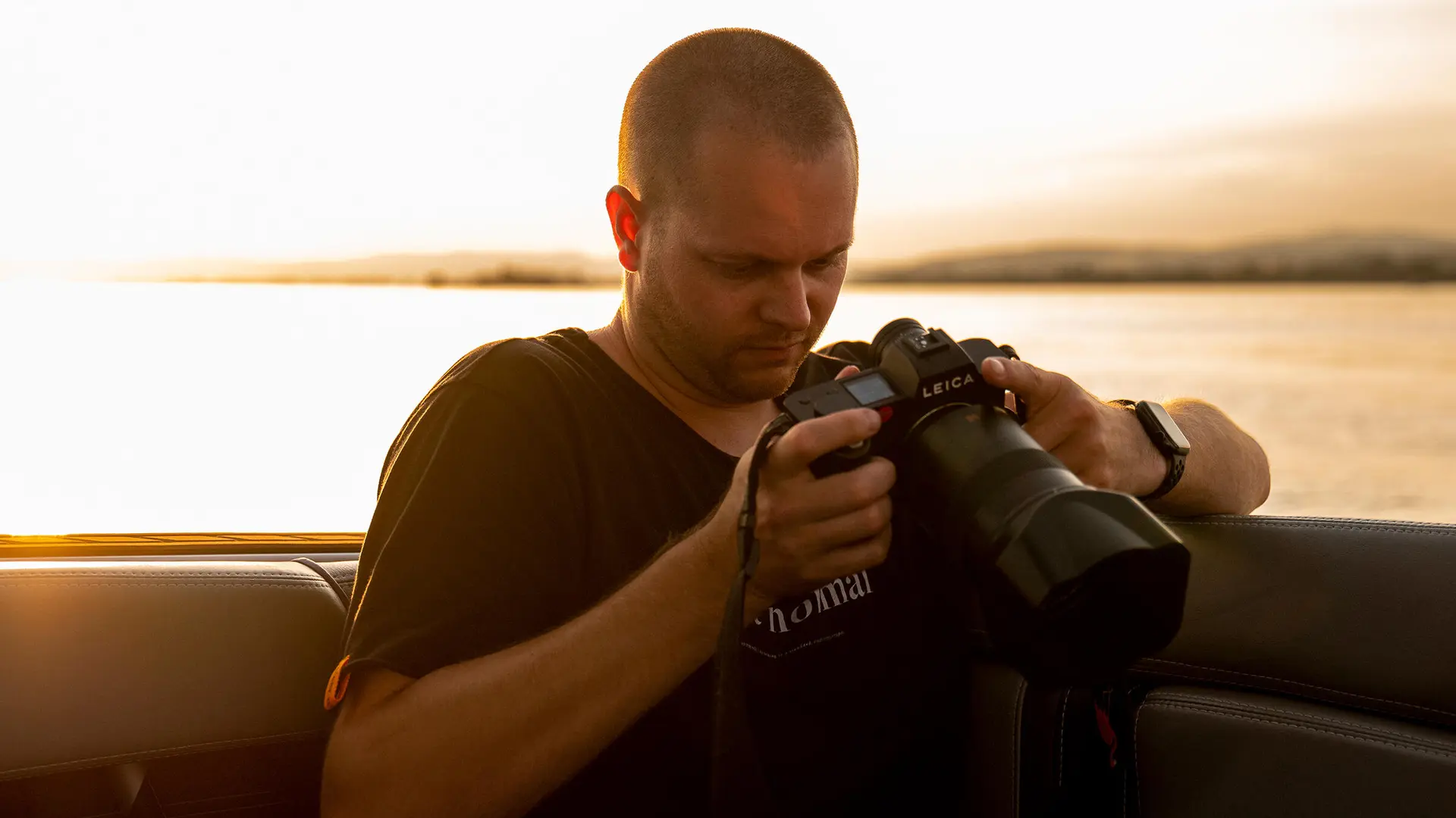 Tino Scherer looking at his camera. In the background is a sea at sunset.