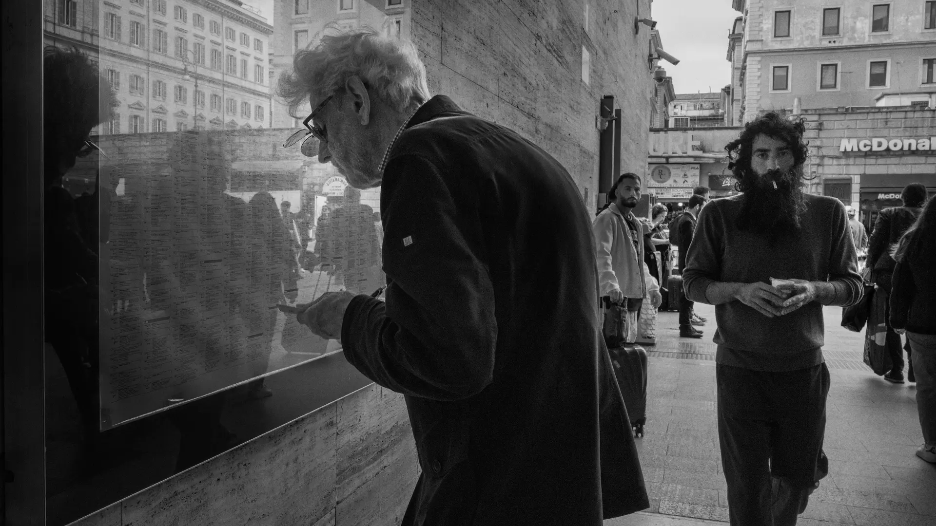 Elderly man in the city looking at a train timetable behind a pane of glass.