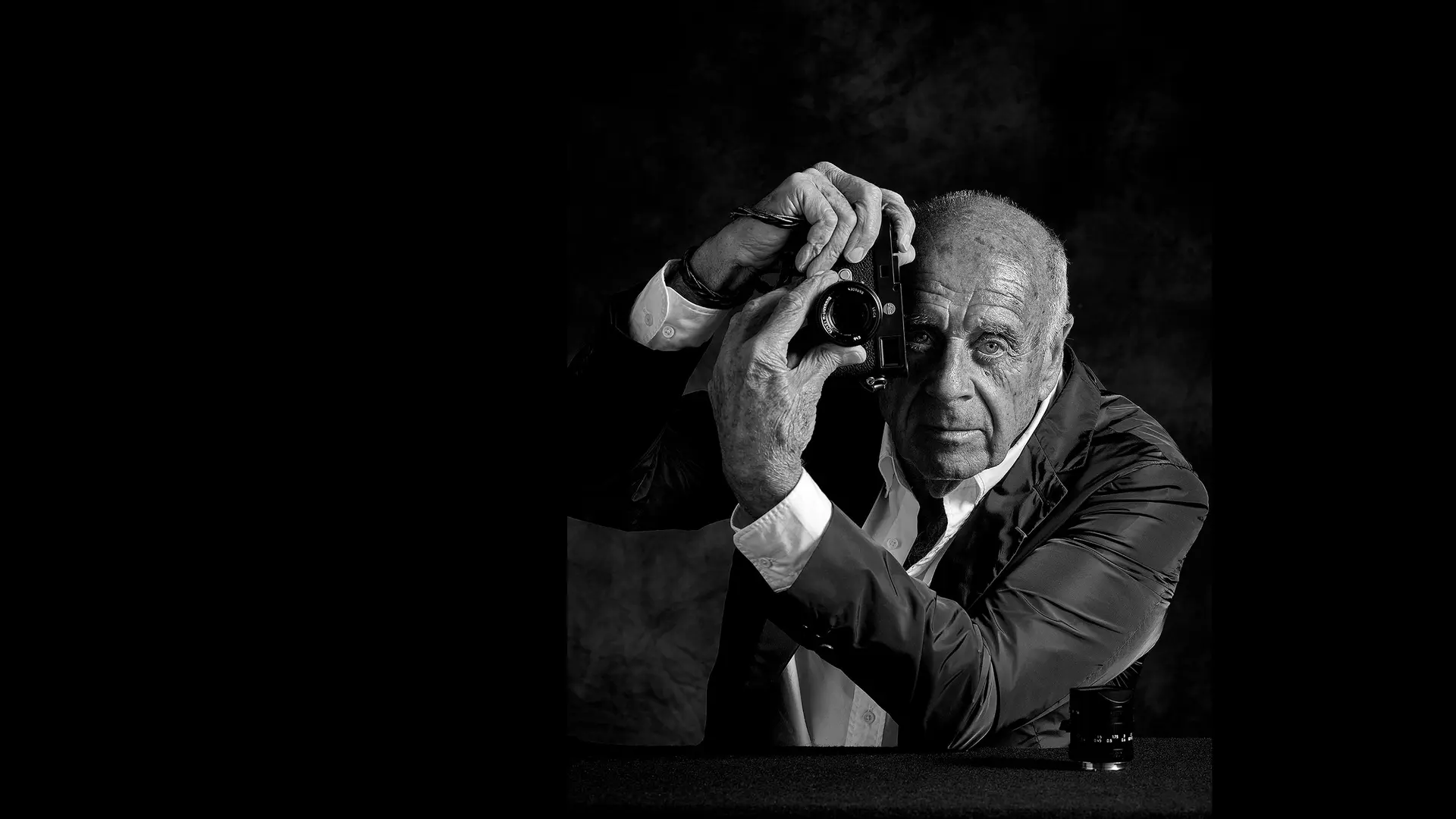 Elderly man holds a camera in front of his face and turns the lens of the camera.
