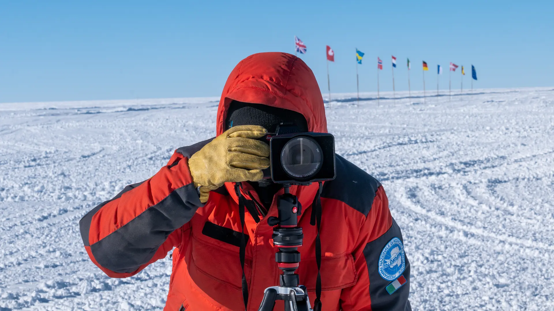 Person takes a photo in a snowy landscape with European flags in the background.