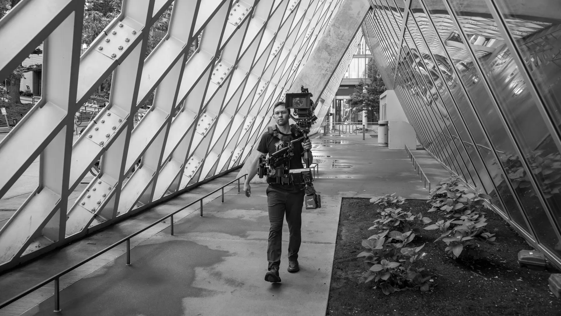 A cameraman walking with a professional camera setup in an architectural space.