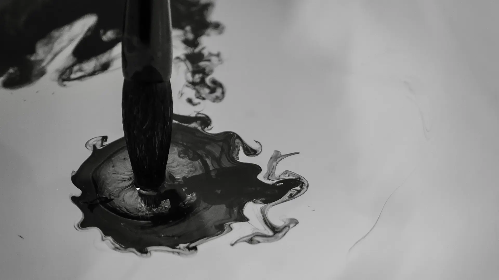 Brush dips into dark ink that spreads in the water.