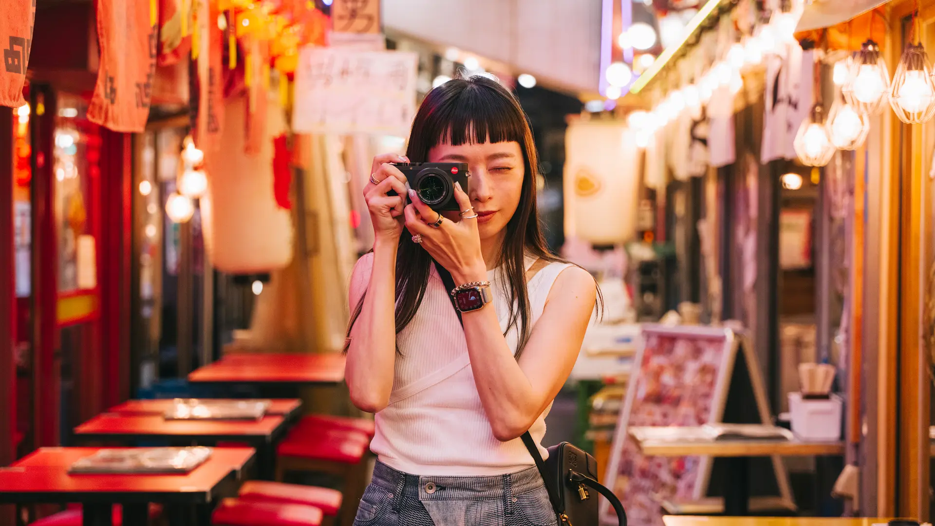 A woman takes pictures with a camera in a colorful, illuminated street.