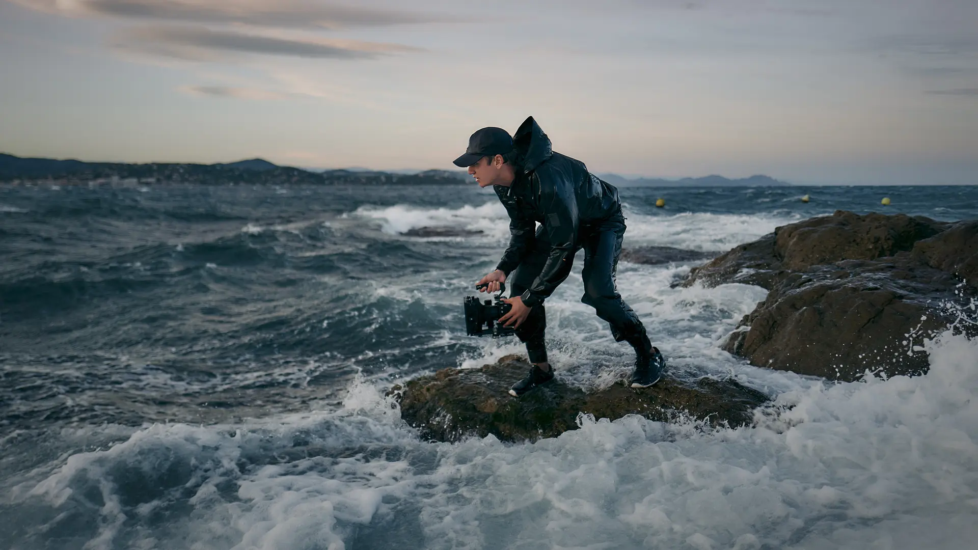 A person is standing on a rock in a stormy sea, holding a pair of binoculars.