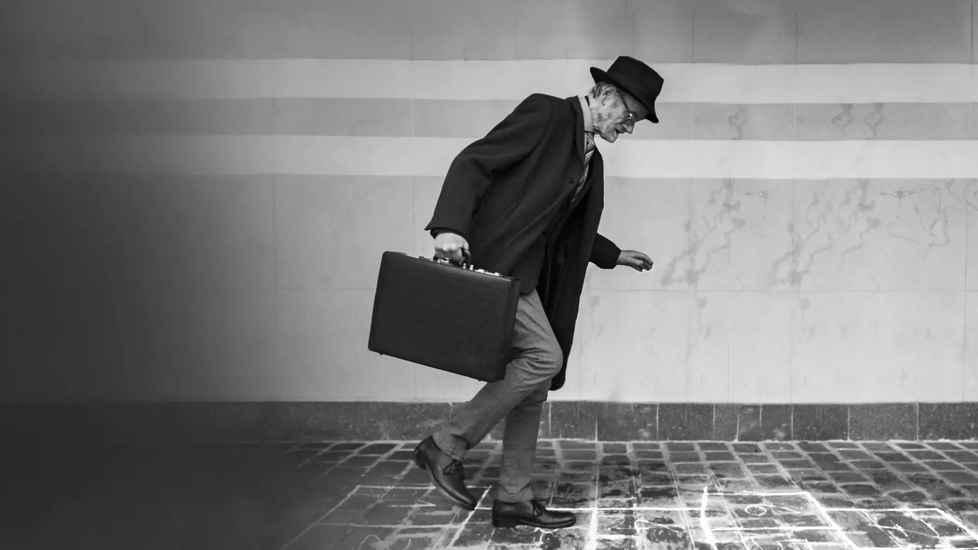 Elderly man in suit with hat and briefcase walking on icy cobblestones.