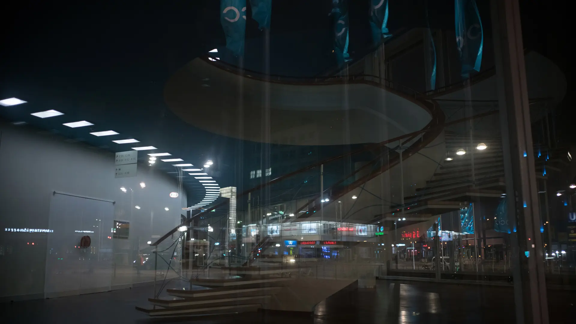 Reflection of a spiral staircase and a city at night in the glass front of a building.