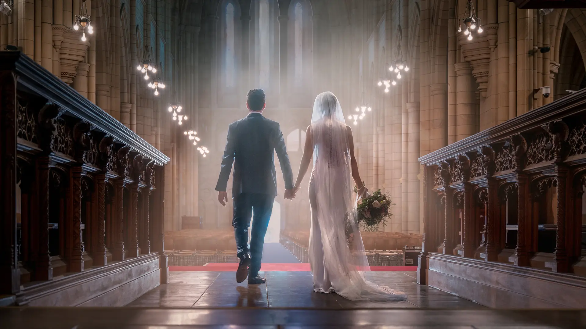A bride and groom walk hand in hand down the aisle of an impressive church.