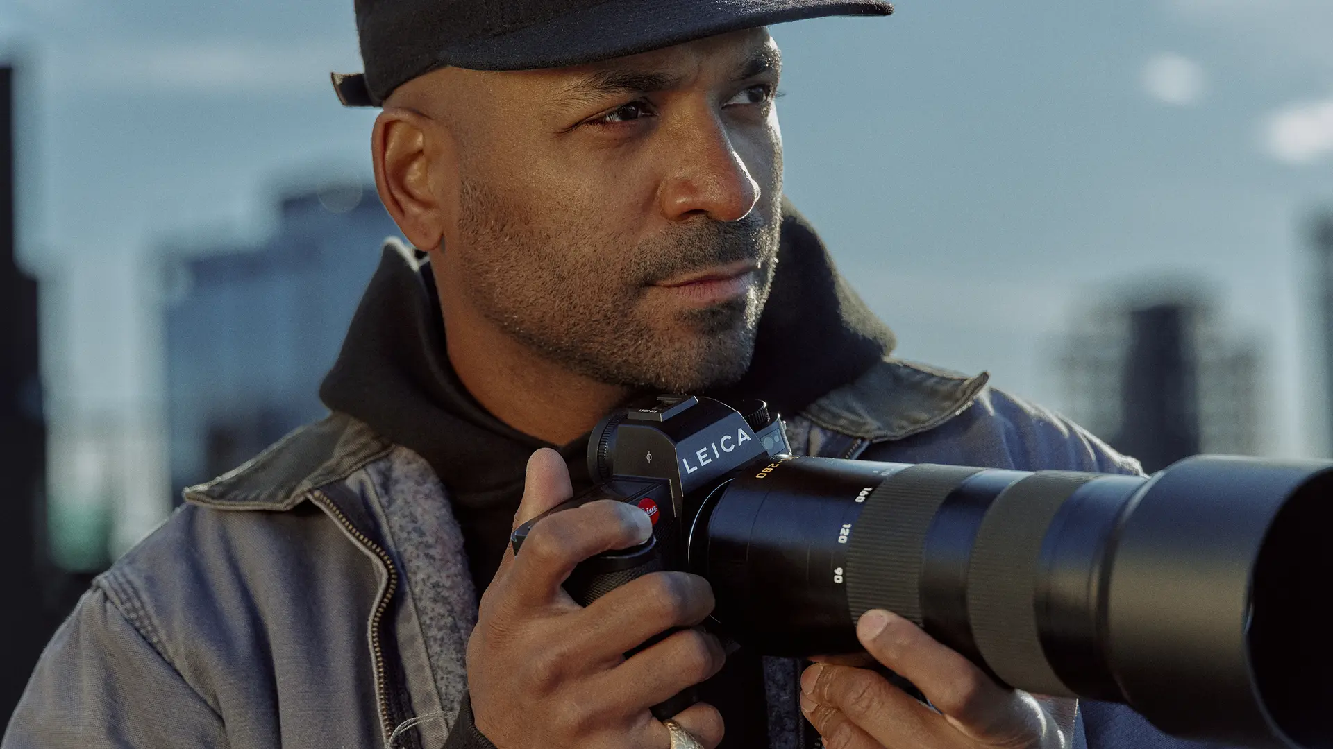 Close-up of a man holding a camera with skyscrapers in the background. 