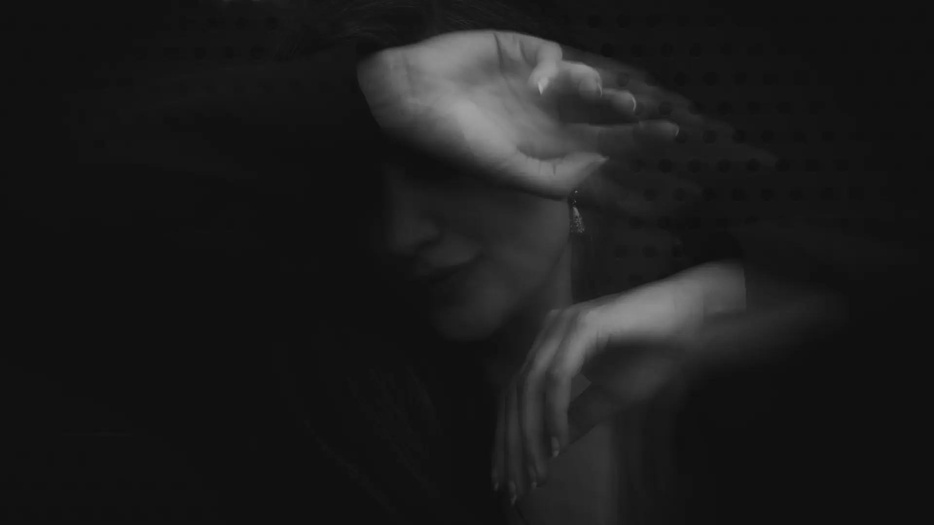 Blurred black and white image of a person covering her face with her arm.