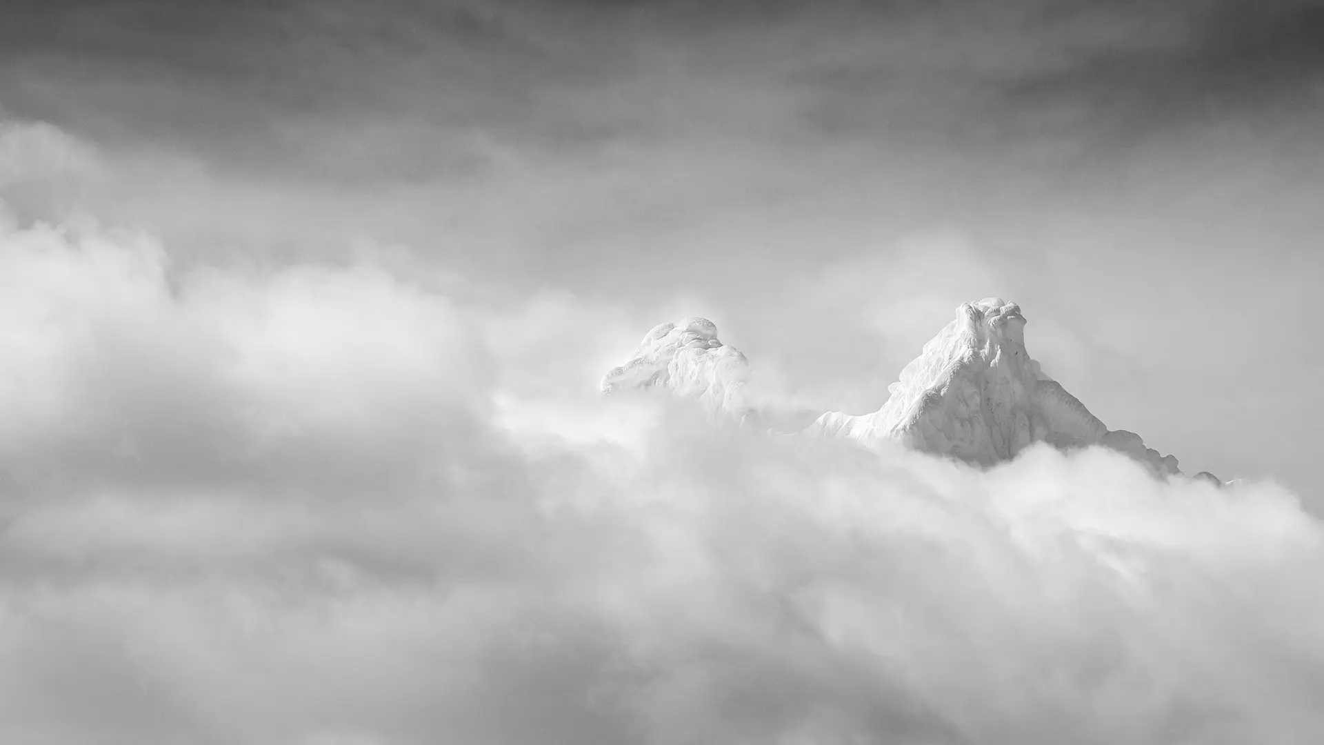 Two snow-covered mountain peaks protrude through a blanket of cloud.