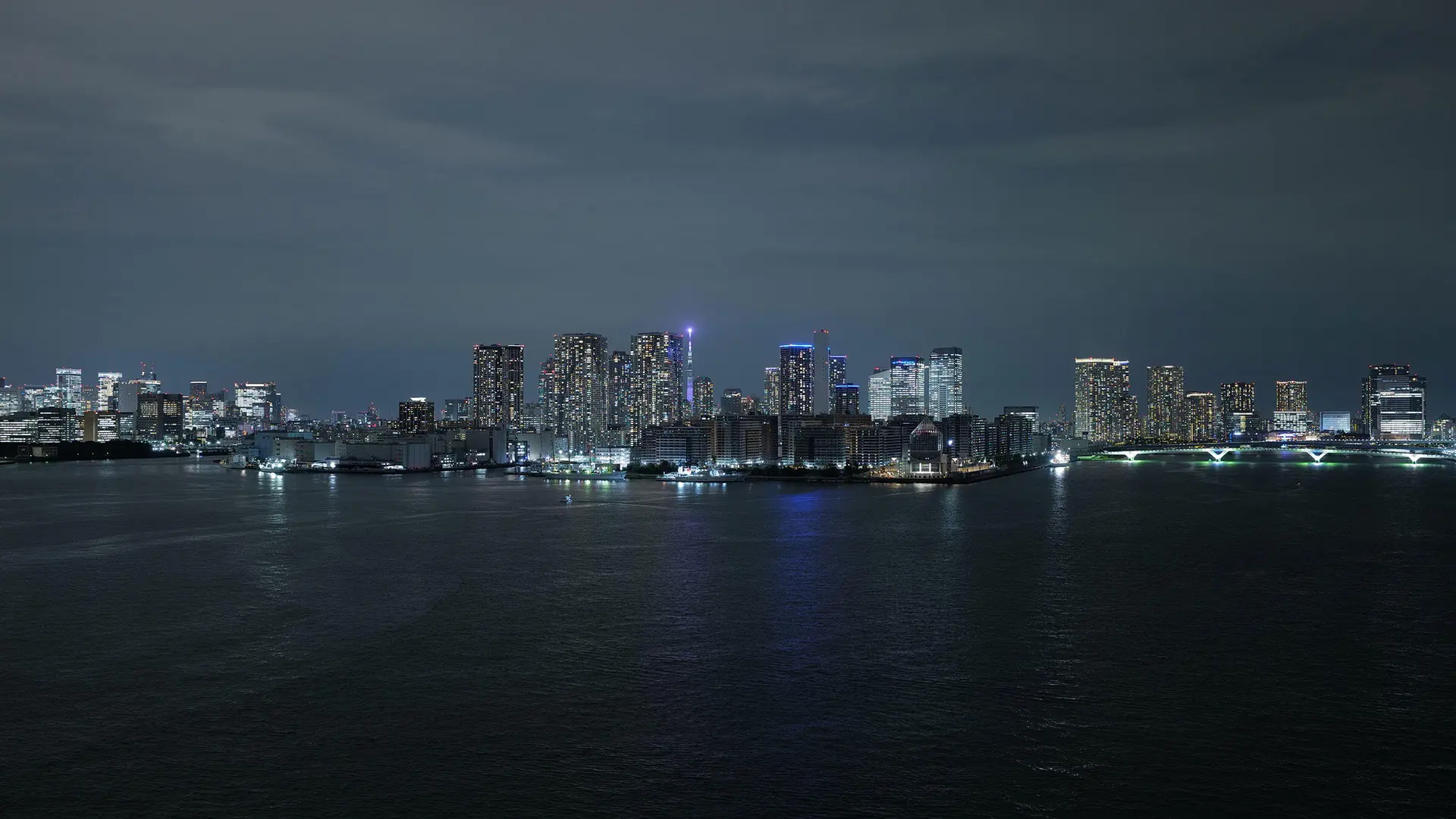 Illuminated skyline of Tokyo at night, with a view of the water in the foreground.