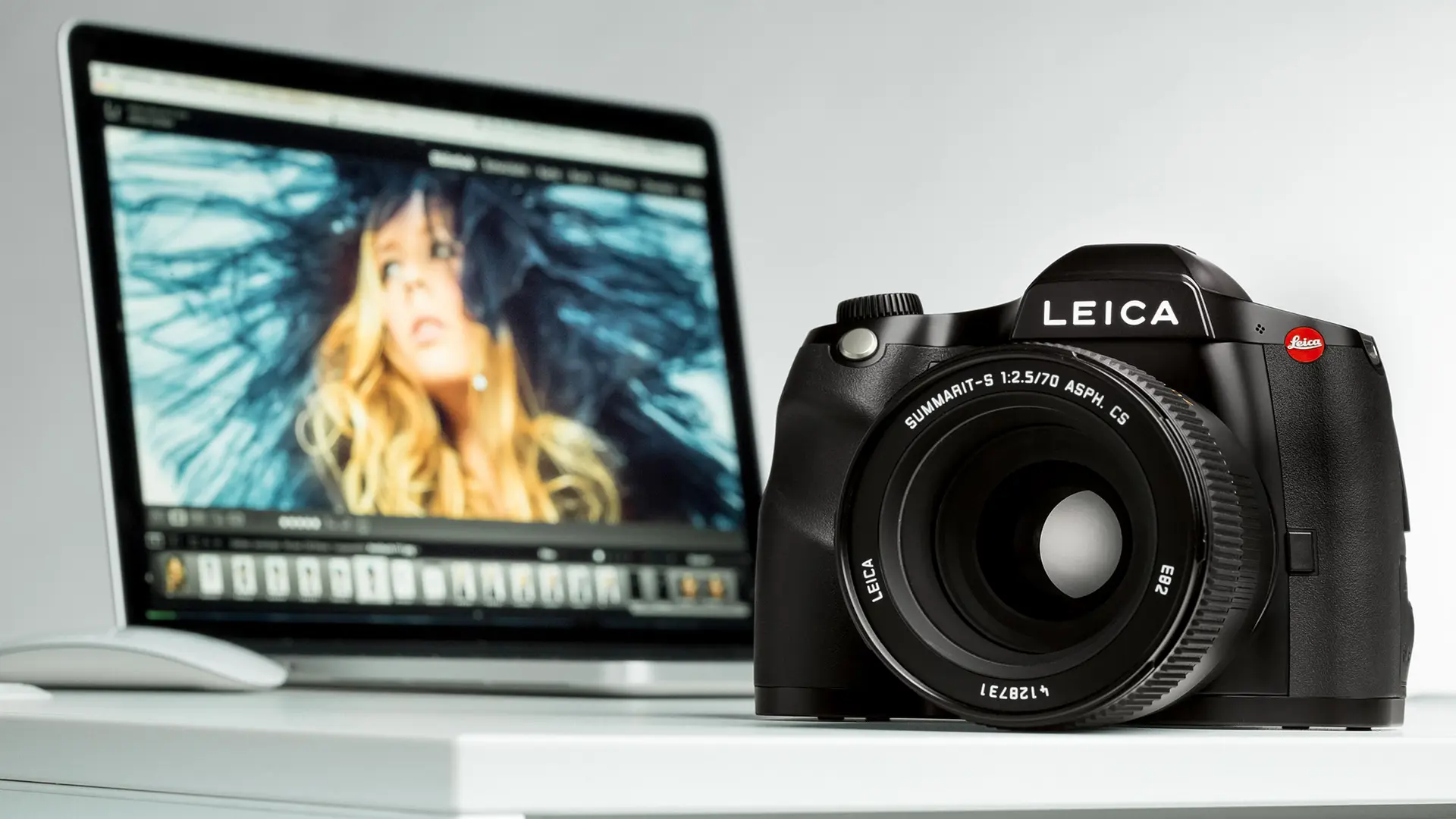 Leica camera on a table in front of a laptop showing a portrait photo.