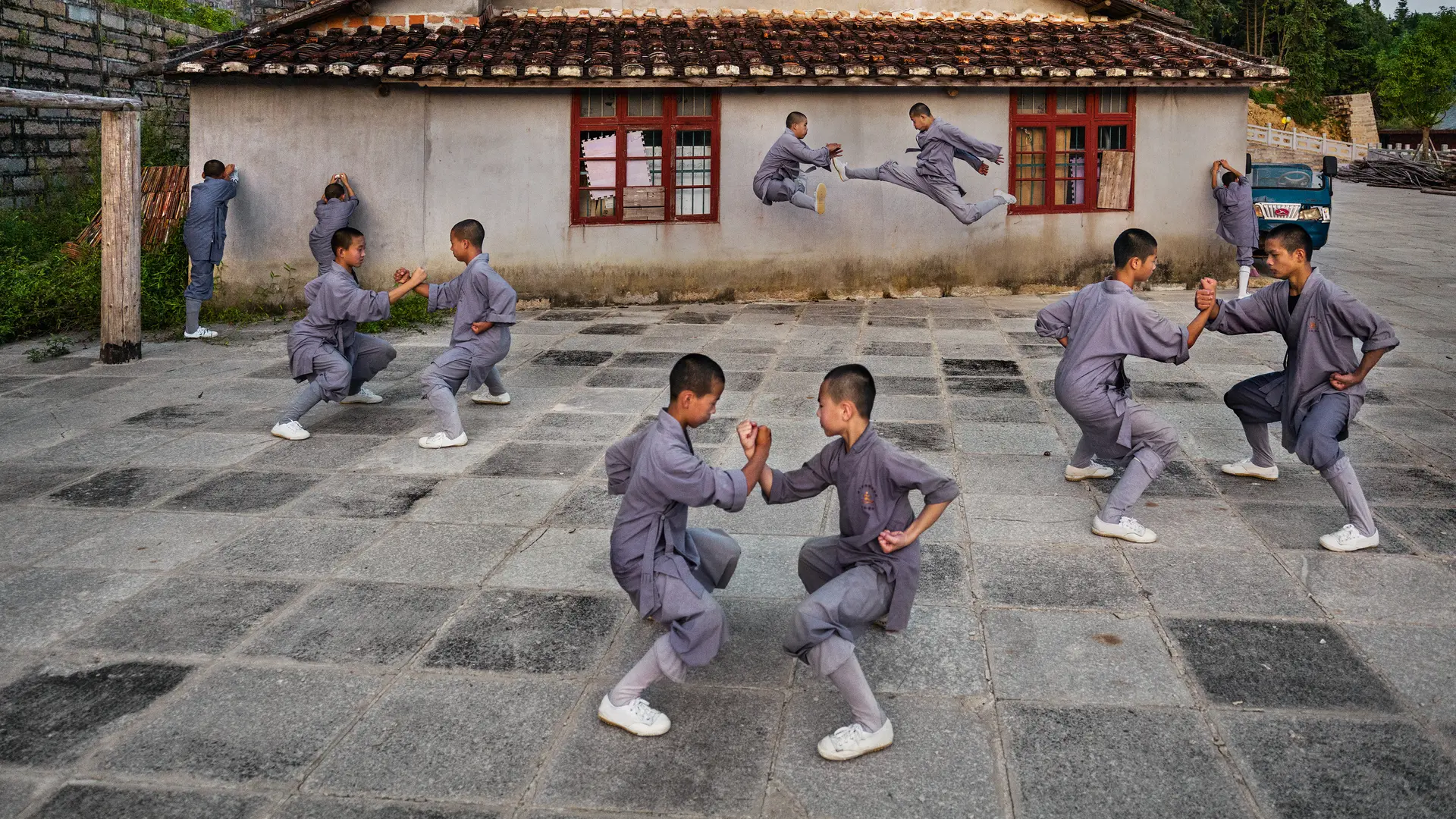 Shaolin monks practise martial arts in the courtyard in front of a traditional building