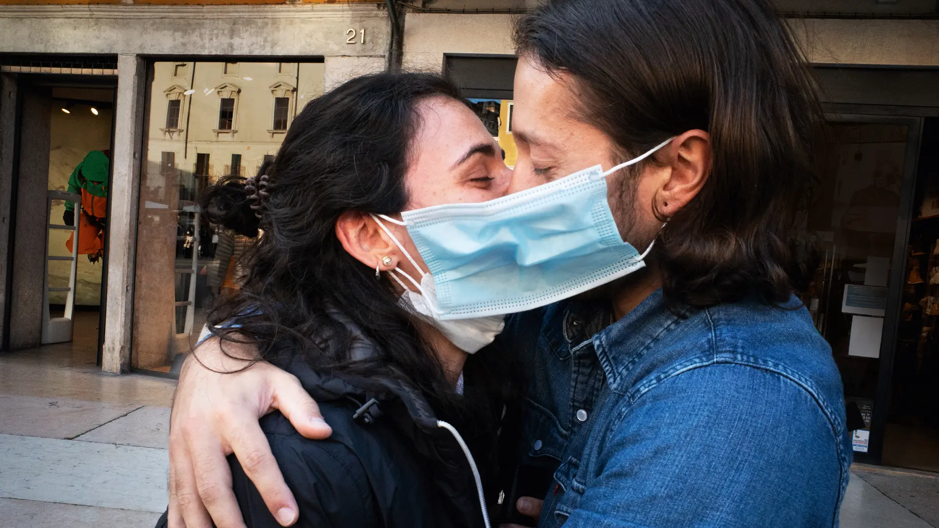 A couple wearing face masks hug and kiss in a street