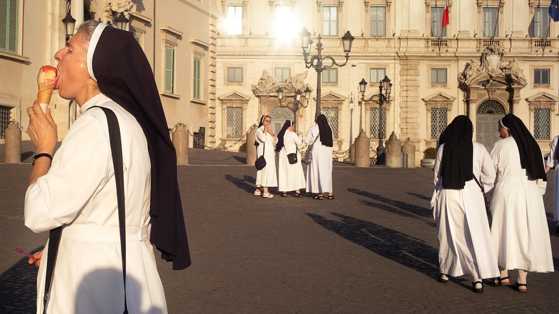 A nun eats an ice cream while several nuns talk in the background.