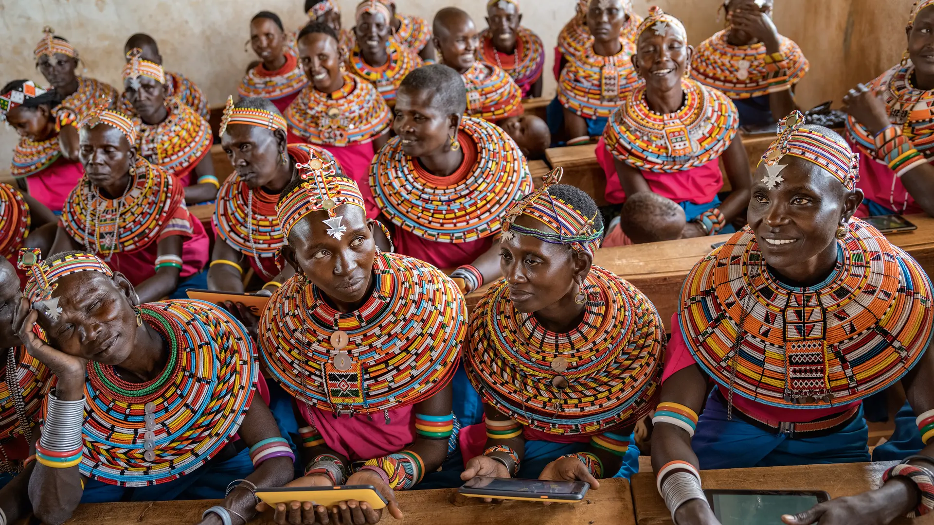 Women from the Samburu tribe in Kenya sitting on a wooden bench in traditional clothes and smiling.