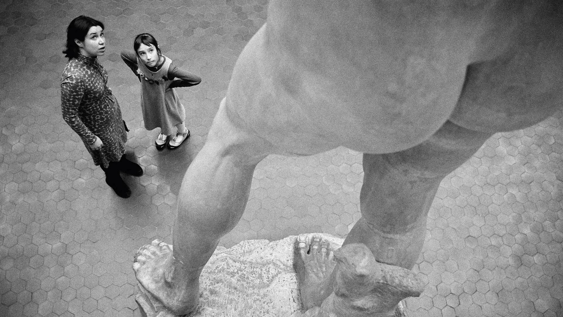 Two people stand in front of a large statue and look upwards.