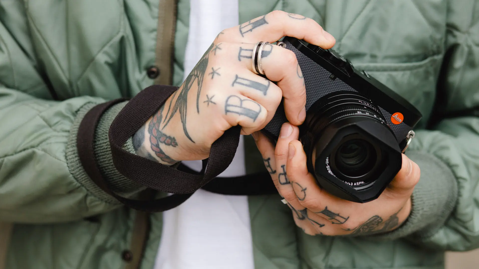 The Leica Q3 43, held by a man with lots of tattoos and a green jacket.
