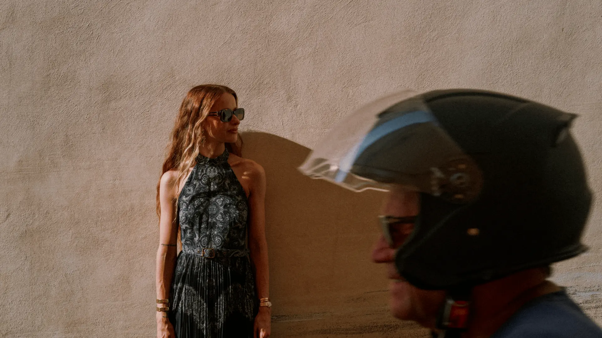 Image of a girl leaning on a wall with a motorcyclist passing by