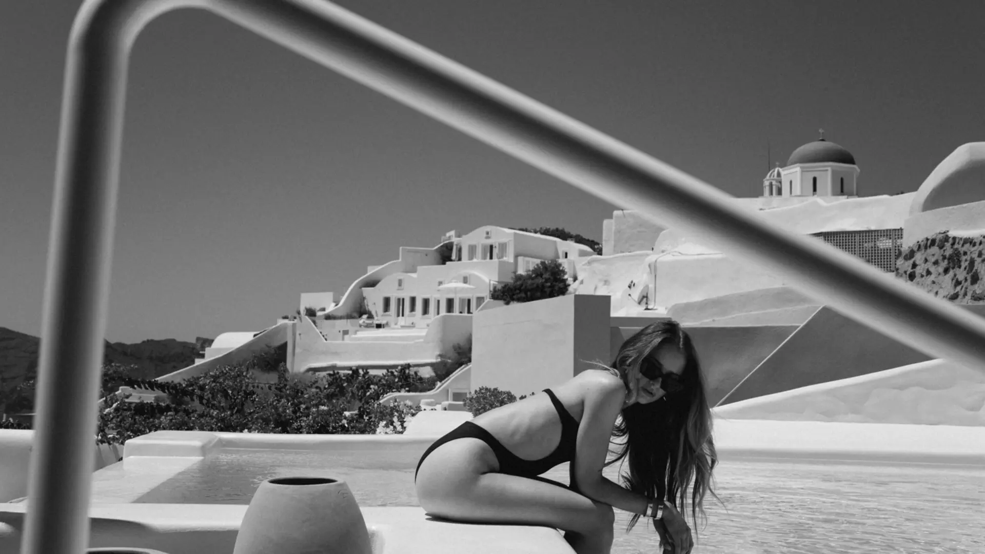 Black and White photograph of a lady sitting next to a swimming pool