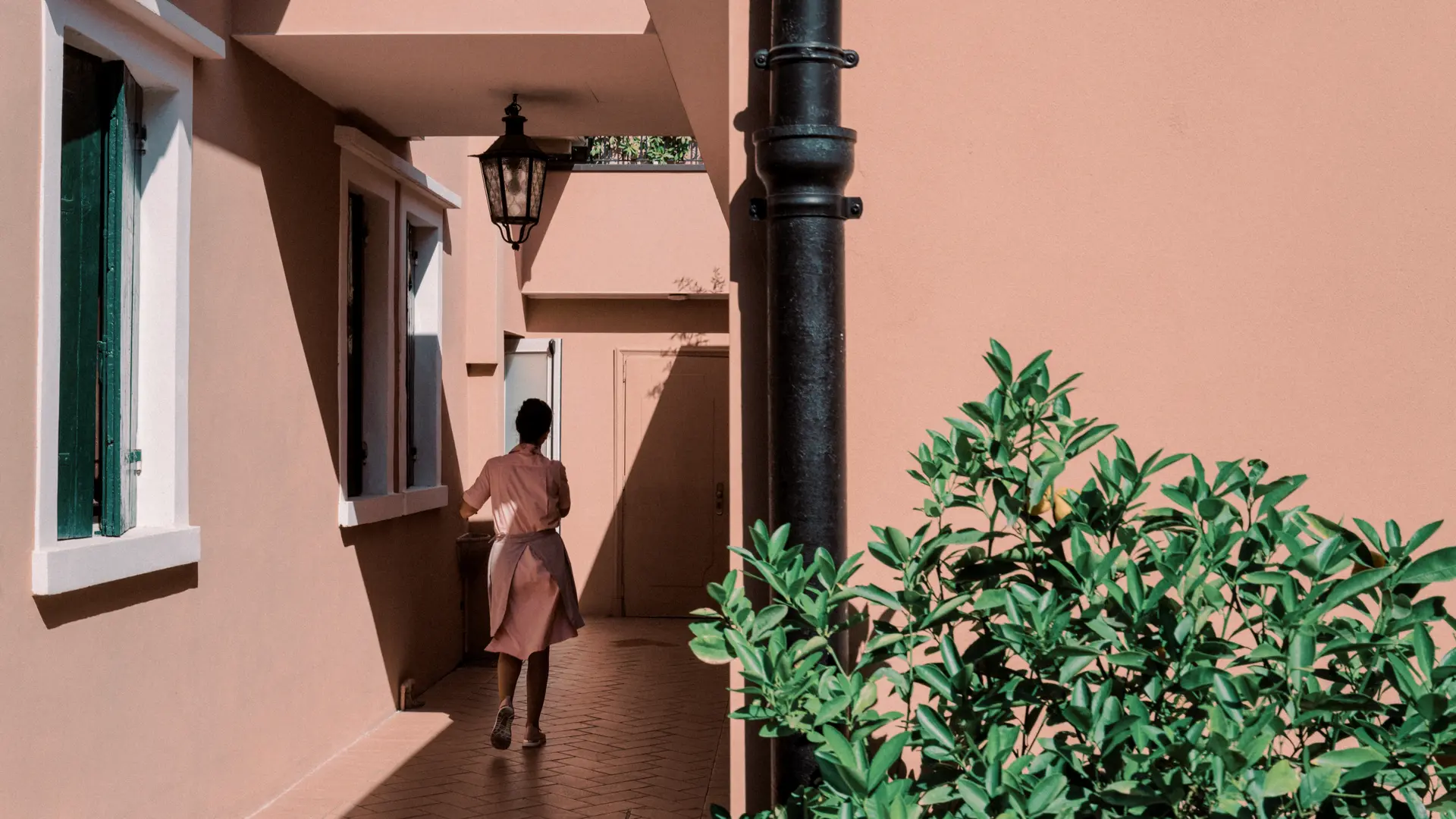 Image of a lady in pink dress by a building with pink paint.