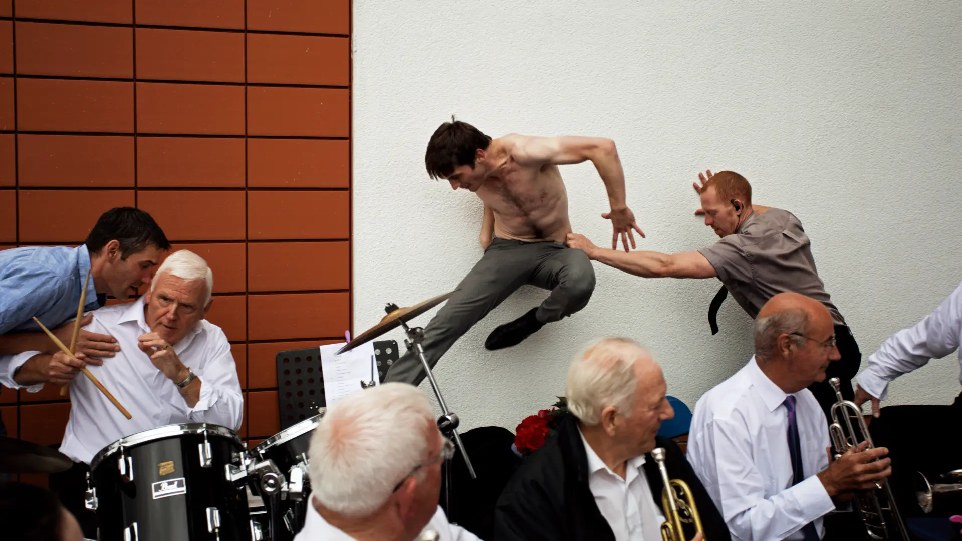 Group of men at a music event. Set on a brick and plain wall.