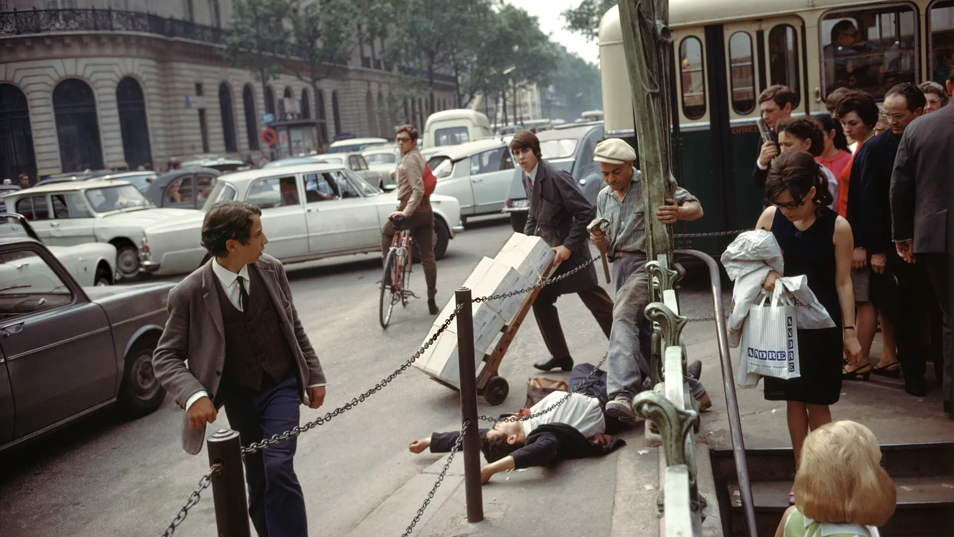 A young man in a suit and tie lies on his back with arms stretched above his head, directly next to the metro station