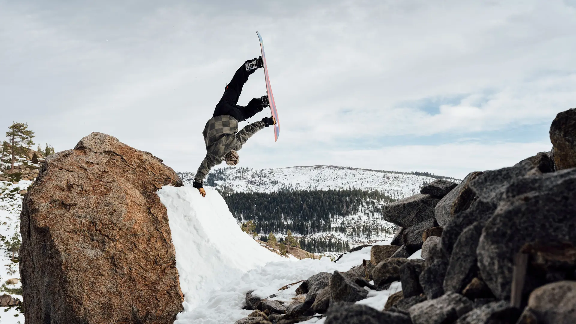 Snowboarder does a one-armed handstand on a ramp in the mountains