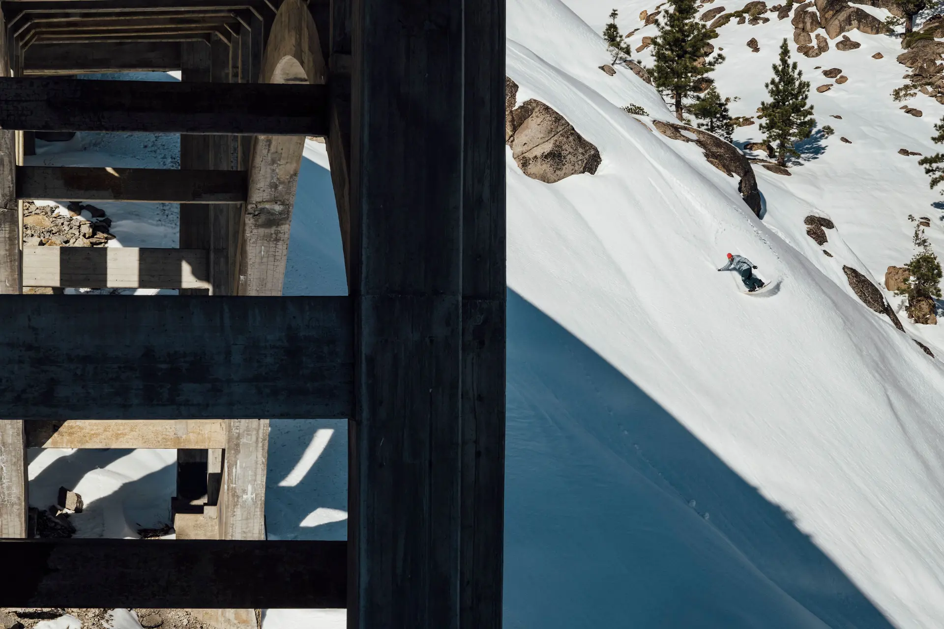 Snowboarder riding in the shadow of a bridge off the track