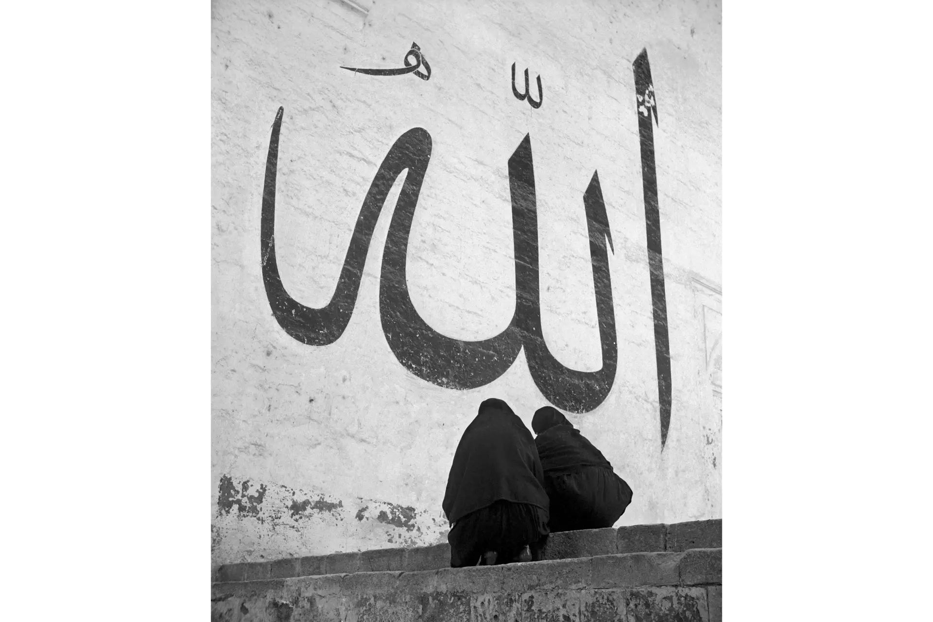 Two veiled people in front of Arabic lettering