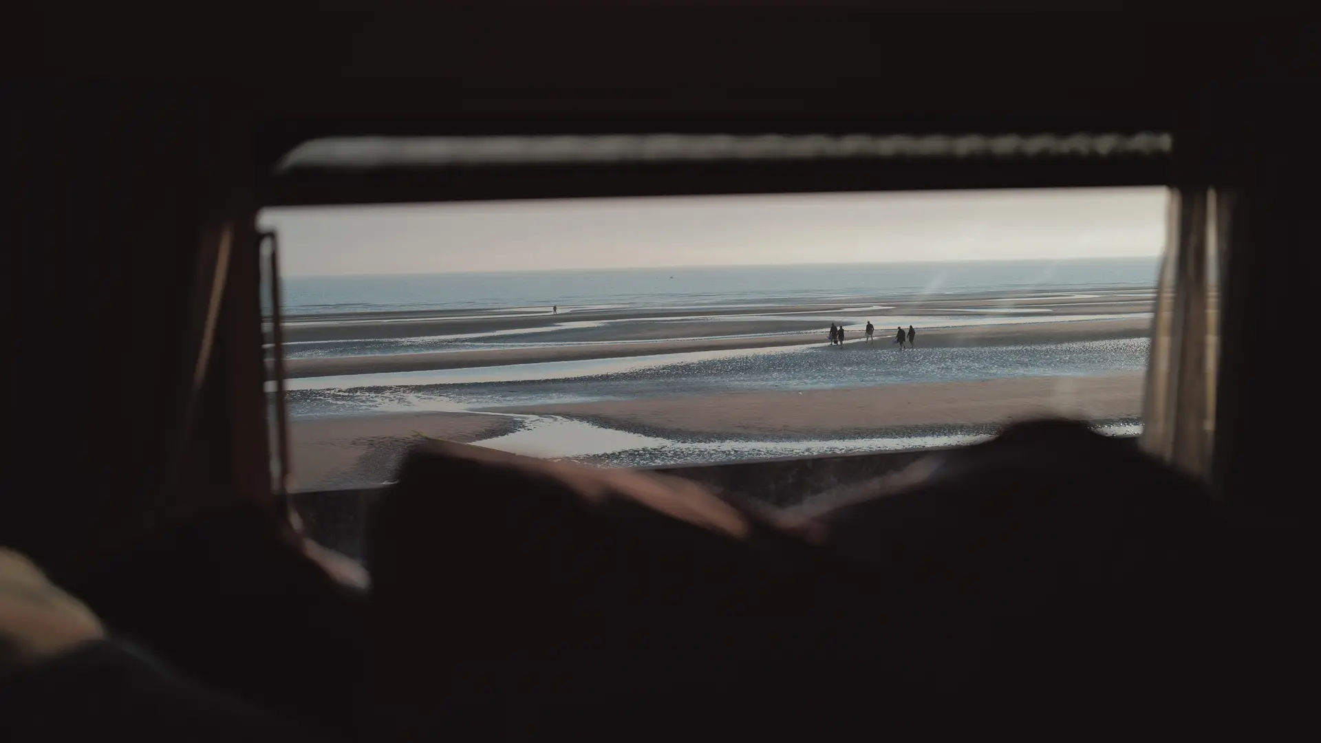 People on the beach photographed from a small window of a caravan