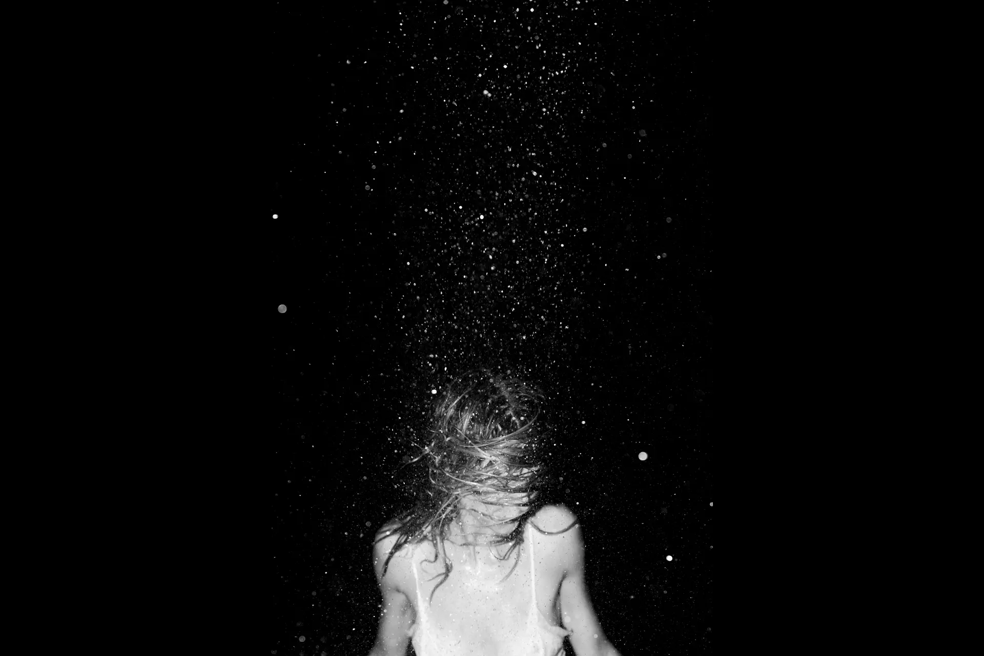 Woman in front of a black background shaking her wet hair