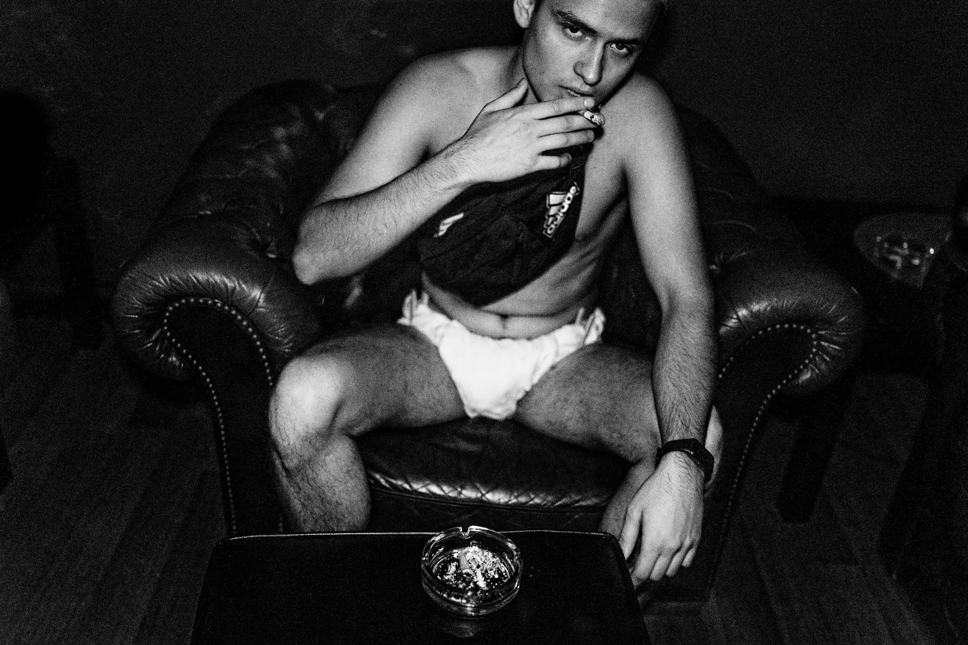 Man sitting on a couch with white pants and cigarette