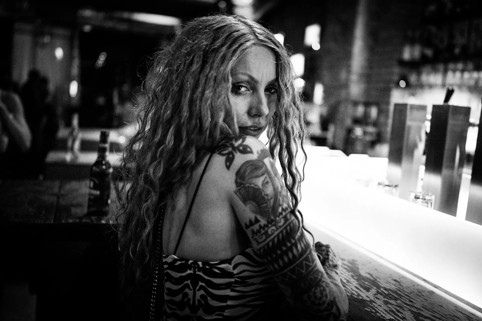 Woman with curly hair and tattooed arm sitting at the bar counter