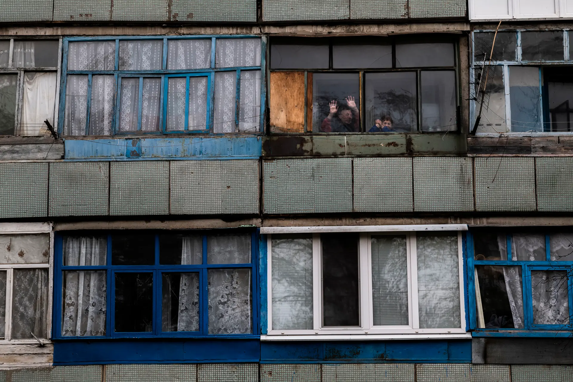 Old married couple standing behind a window in an old block of flats