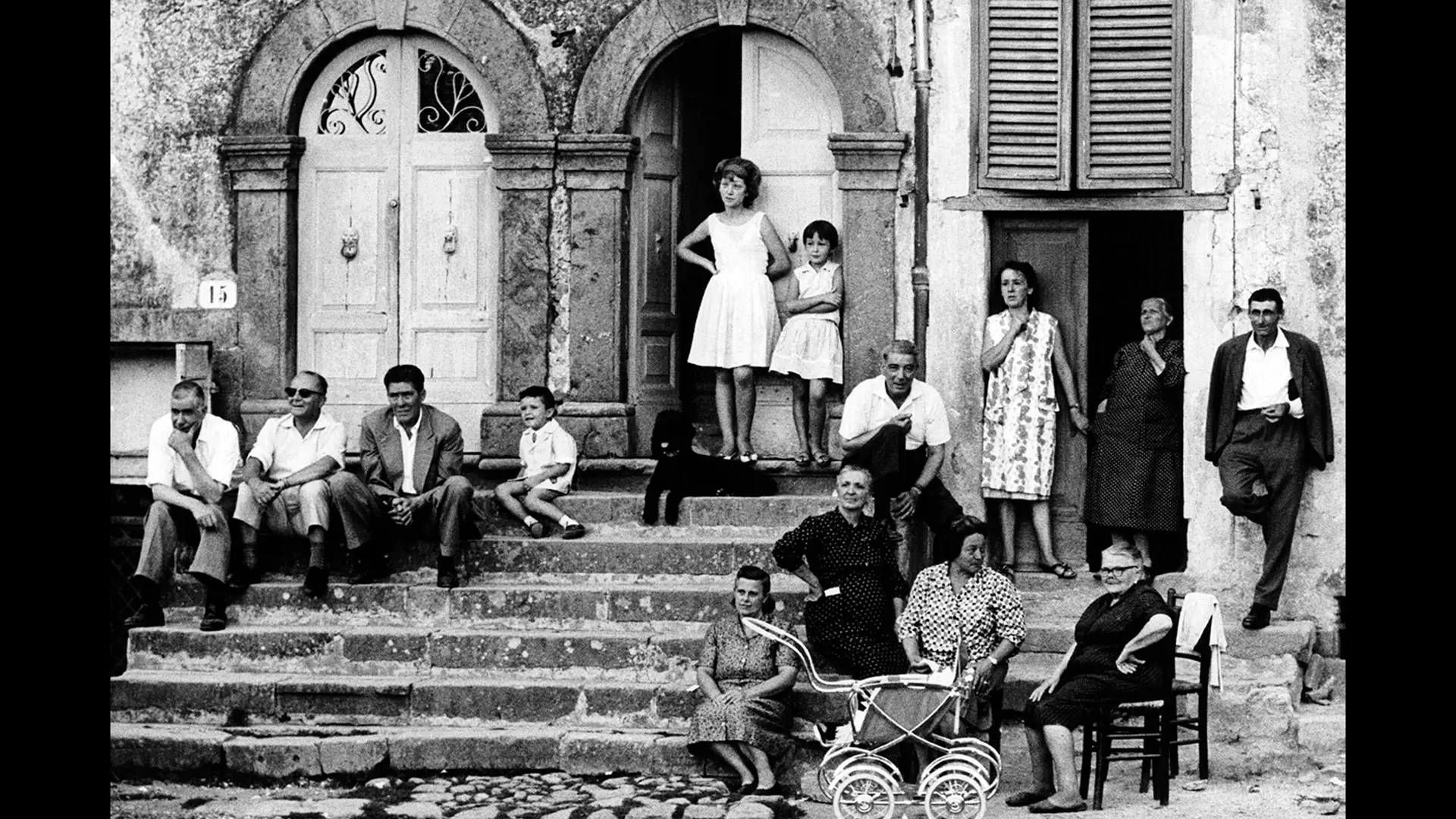 A group of people sitting outside on stairs in front an old house.