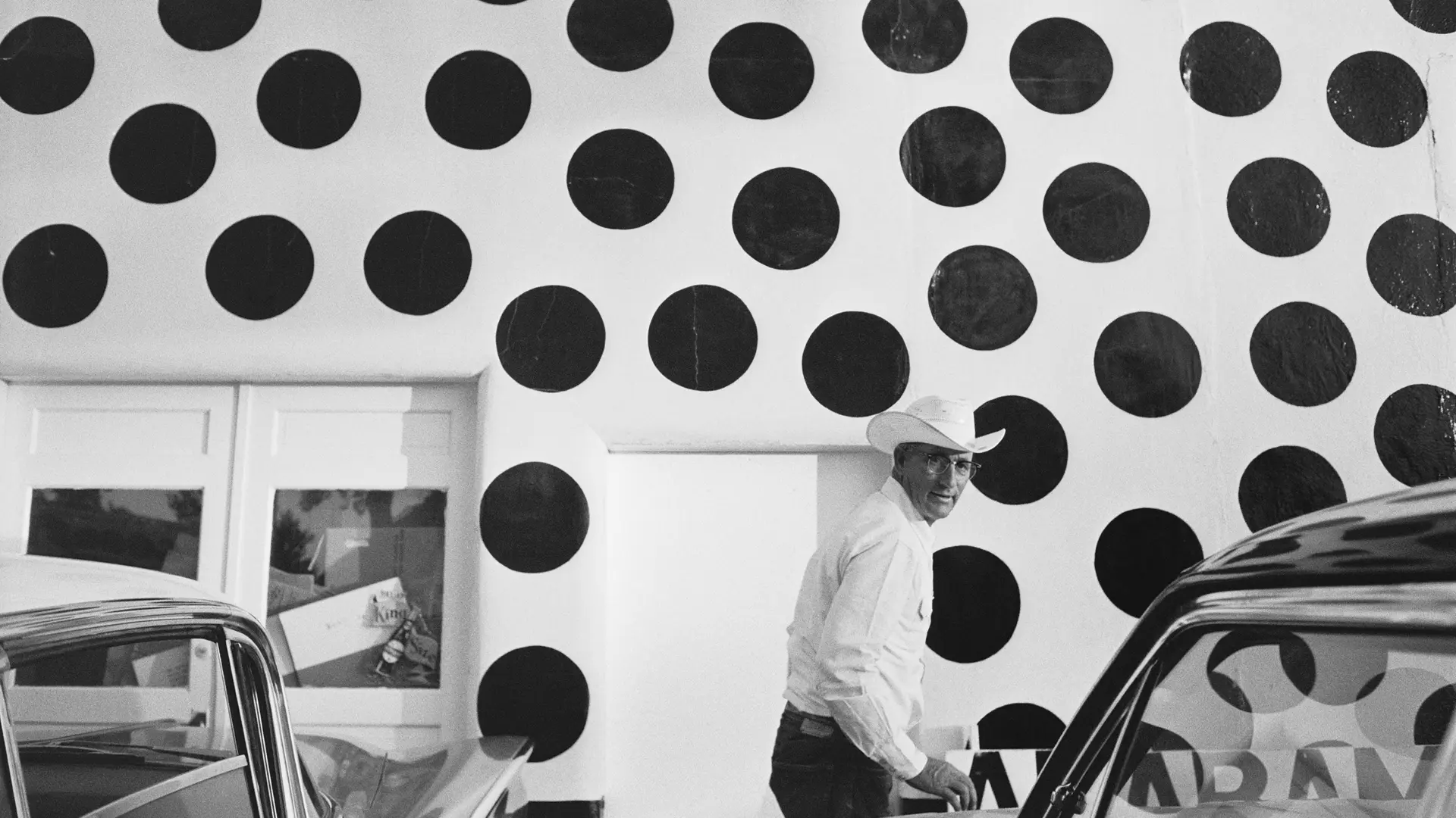 Man with hat in front of a white wall with large black dots