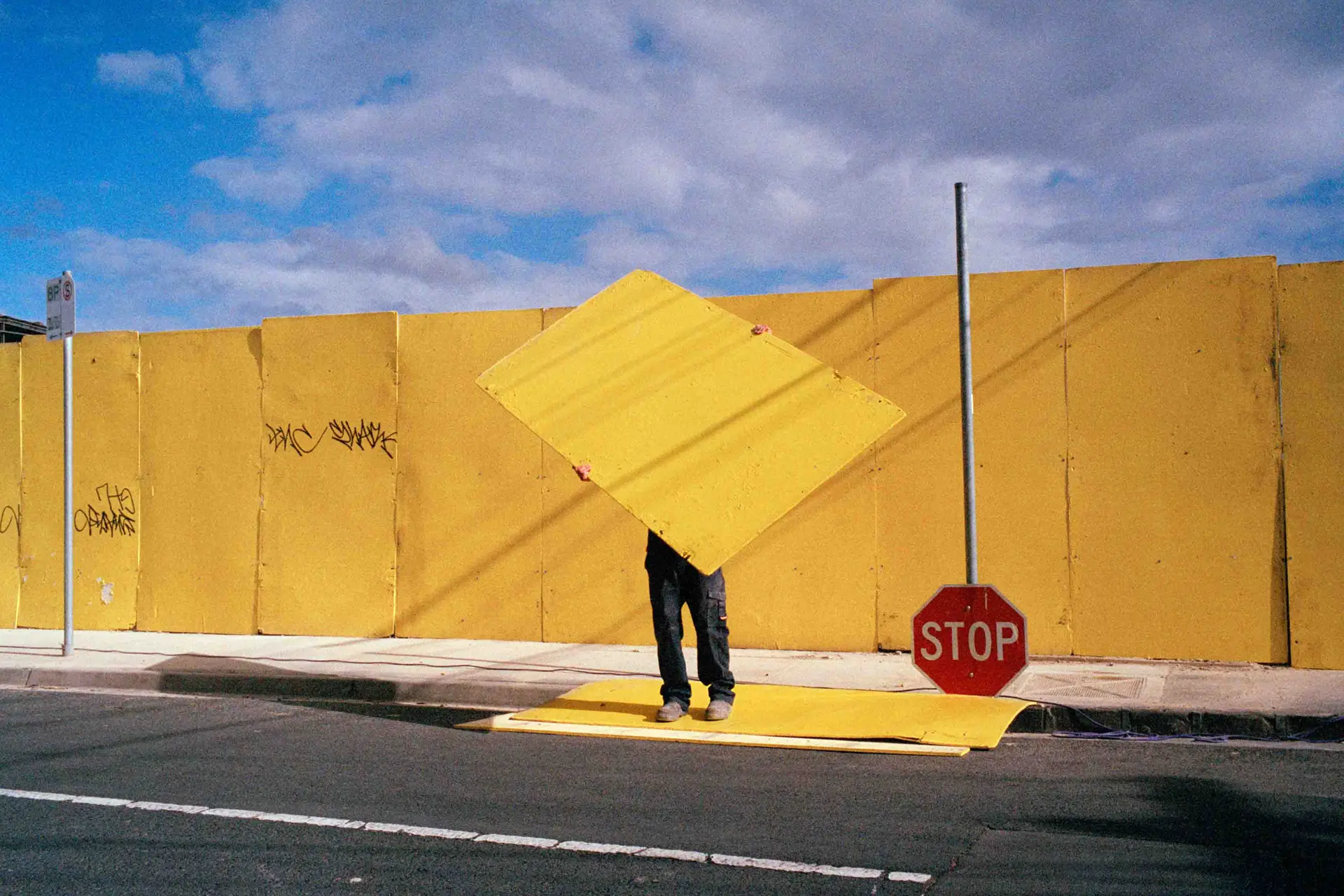 Man holds large heavy yellow plate over his head and stands in front of a yellow wall
